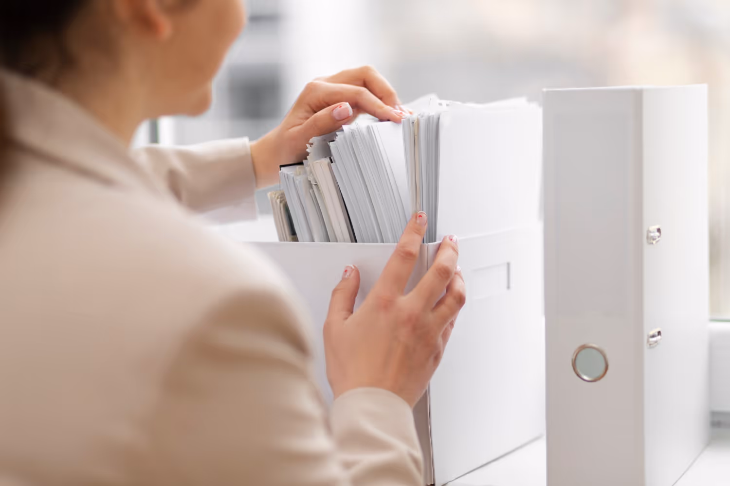 Person organizing white file folders and documents in a white storage box.